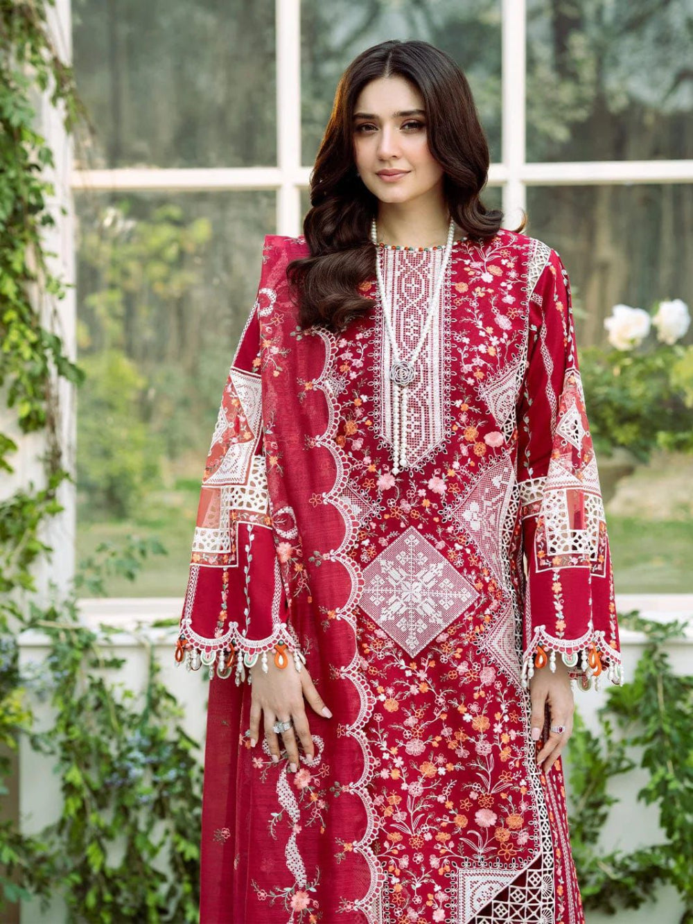 Woman wearing a red embroidered dress with white patterns in an outdoor setting.